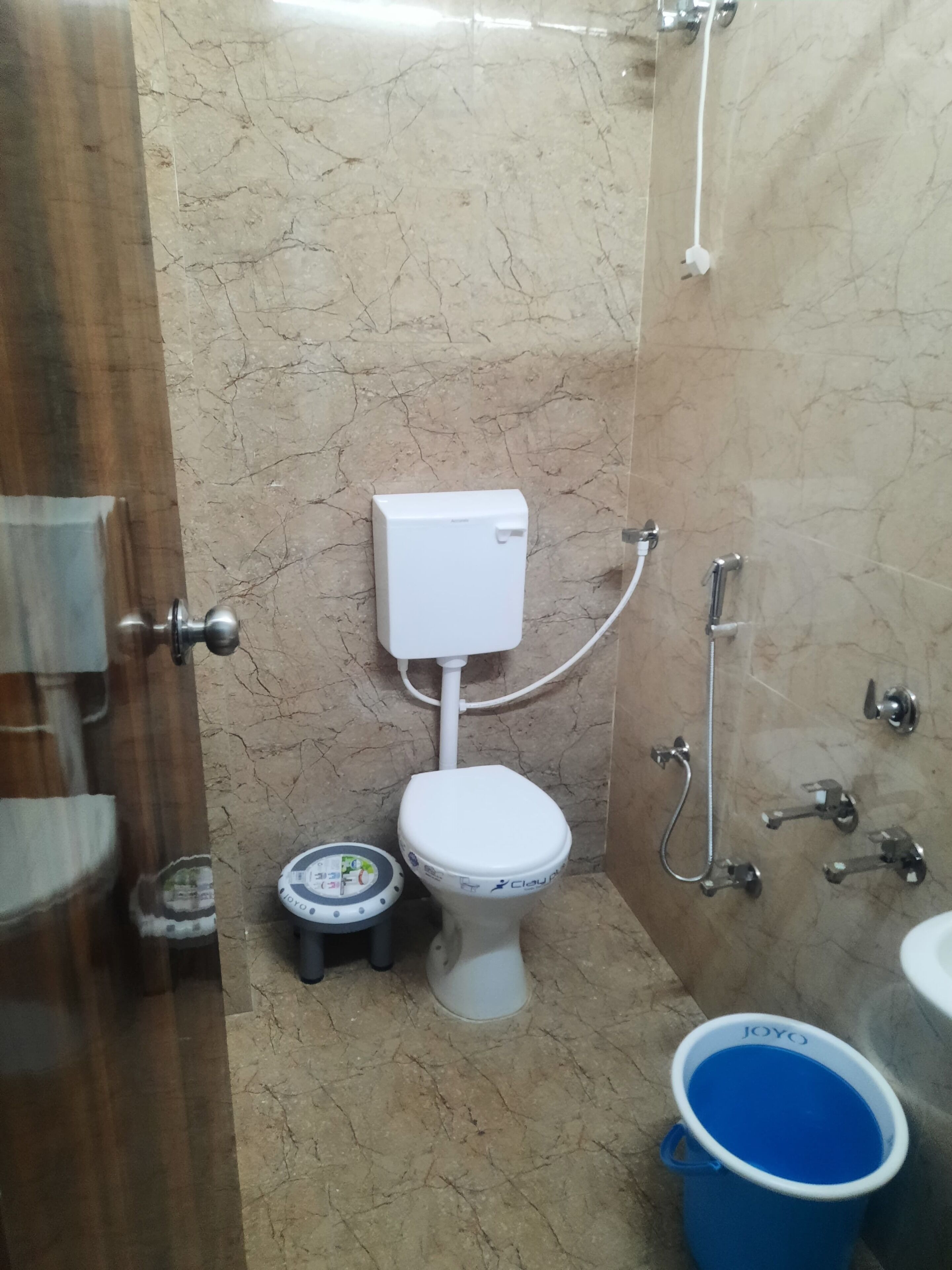 A bathroom with a toilet, a bidet, a small stool, and a blue bucket.