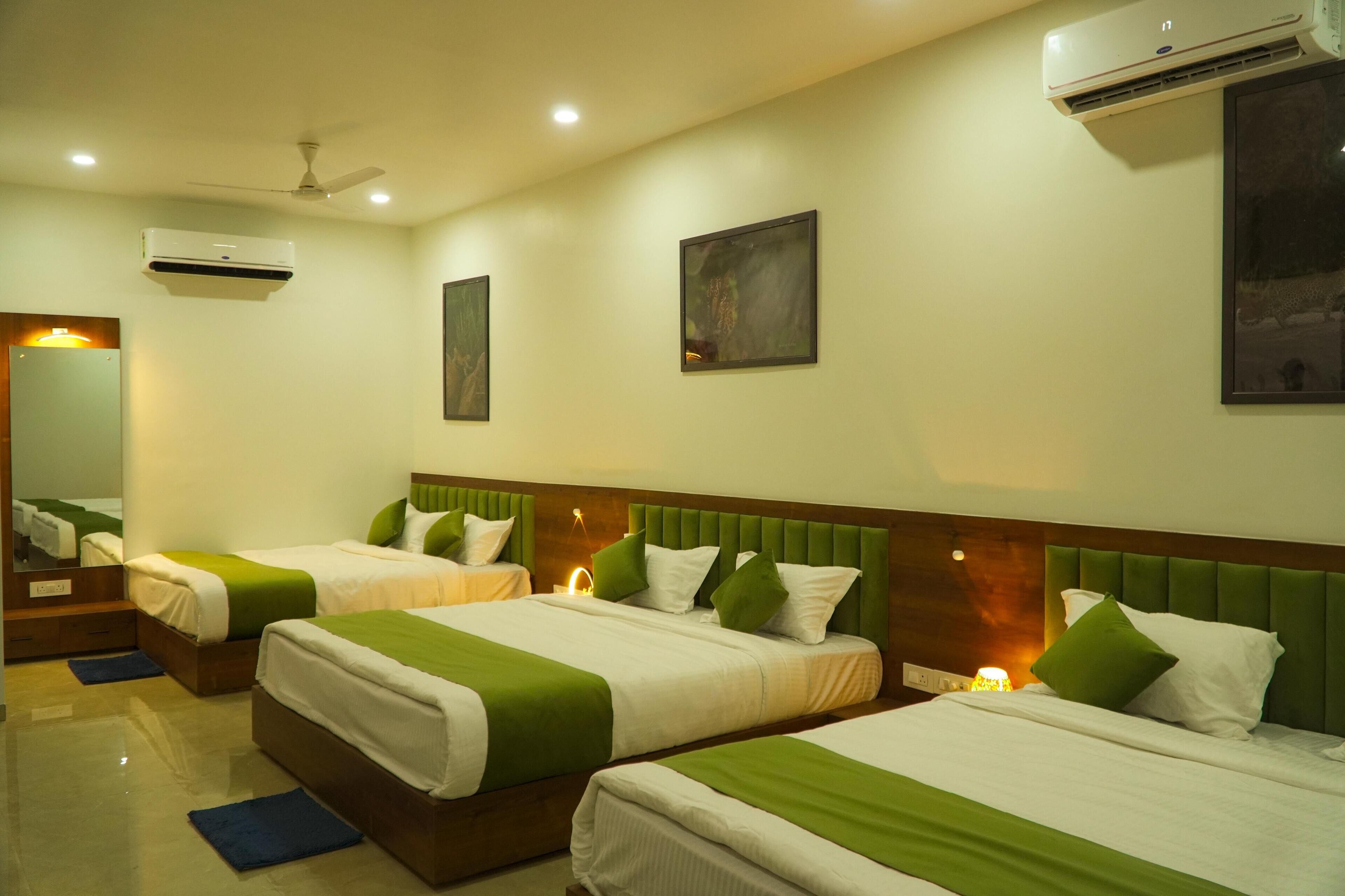 A hotel room with two beds, each with green and white bedding, a ceiling fan, an air conditioning unit, and a nightstand with a lamp.