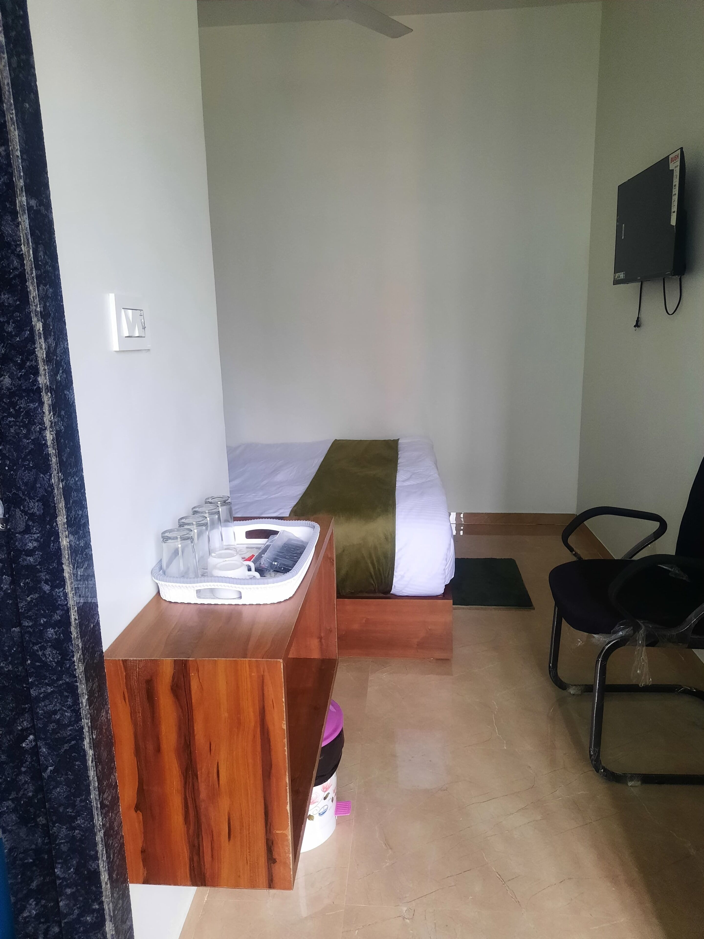 A hotel room with a bed, a wooden desk, a chair, and a television on the wall.