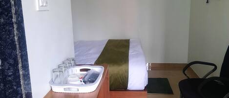 A hotel room with a bed, a wooden desk, a chair, and a television on the wall.