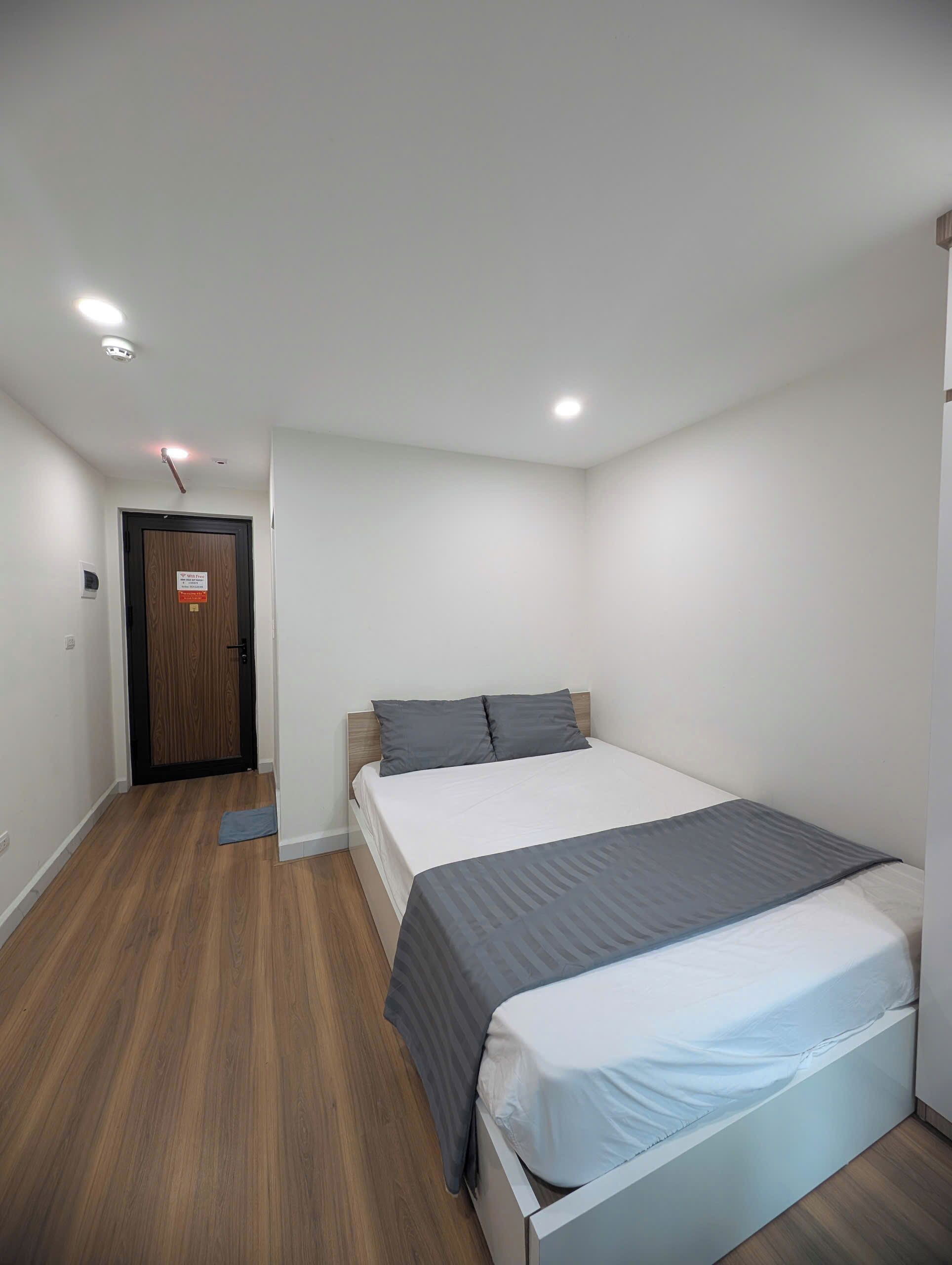 A bedroom with a bed, wooden flooring, a door, and a light fixture.