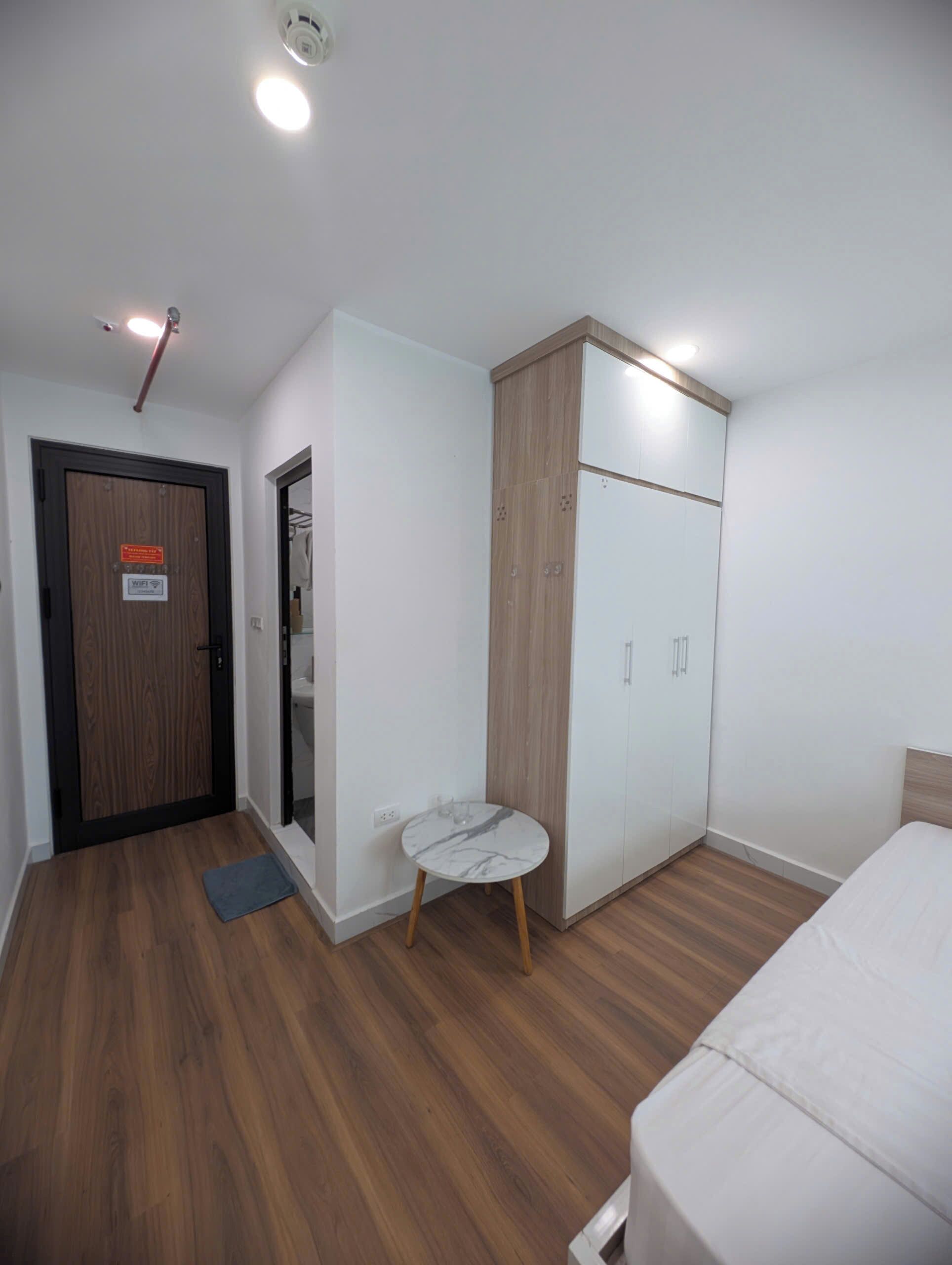 A bedroom with a bed, a wardrobe, a small table, and a door with a sign.