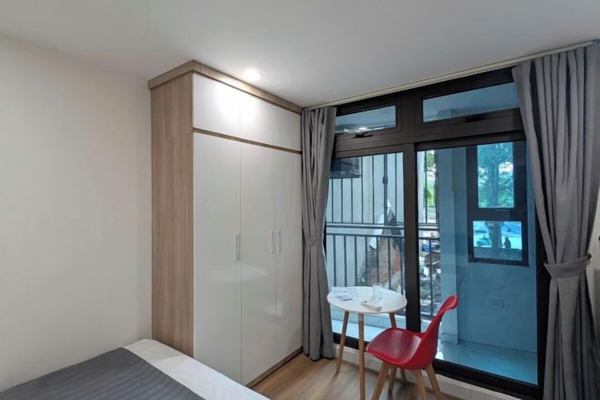 A small room with a bed, a wardrobe, a table with a chair, and a balcony with a view.