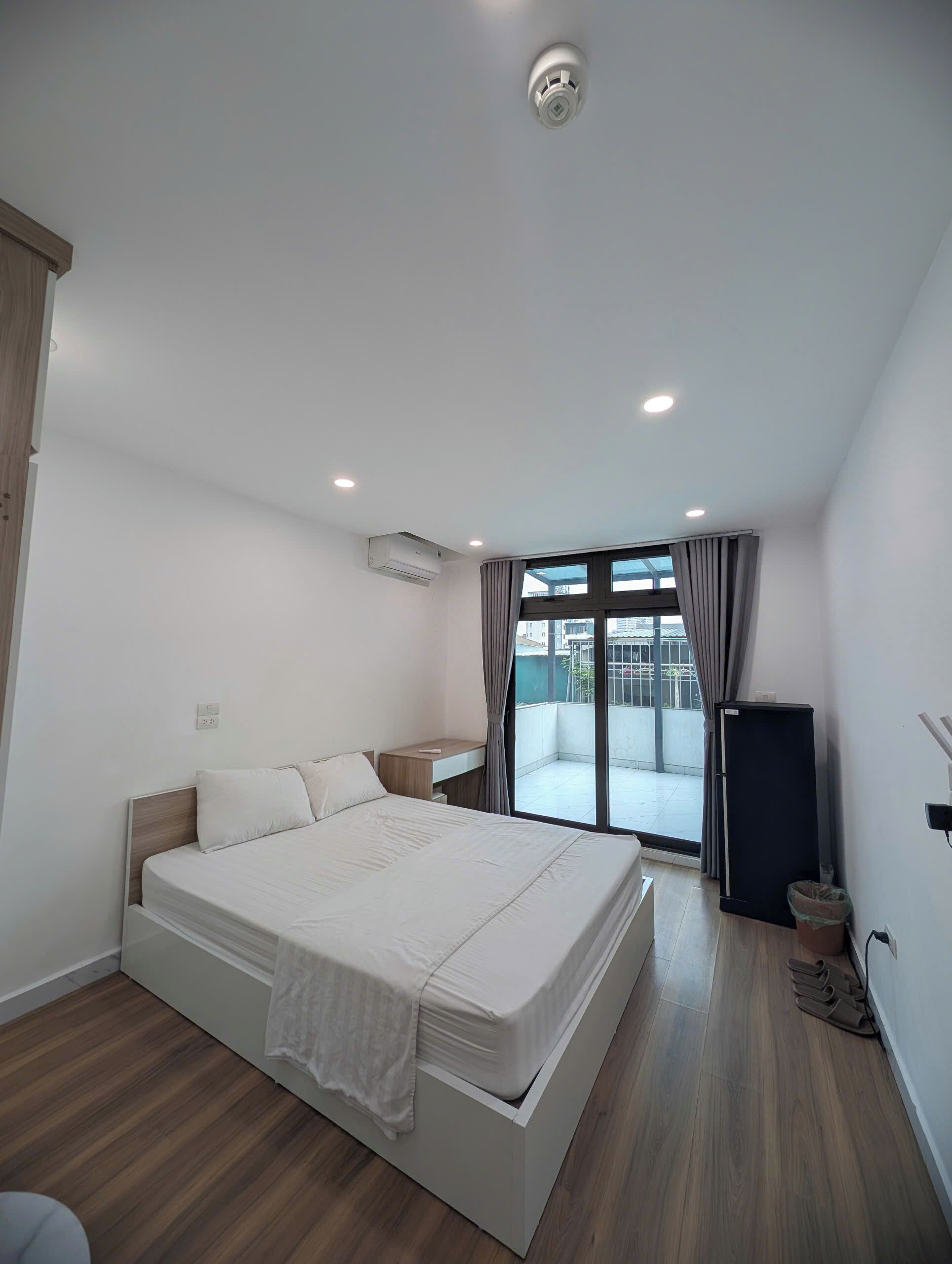 Un dormitorio moderno con una cama grande, un escritorio pequeño, un equipo de aire acondicionado y vistas al exterior a través de un ventanal amplio.