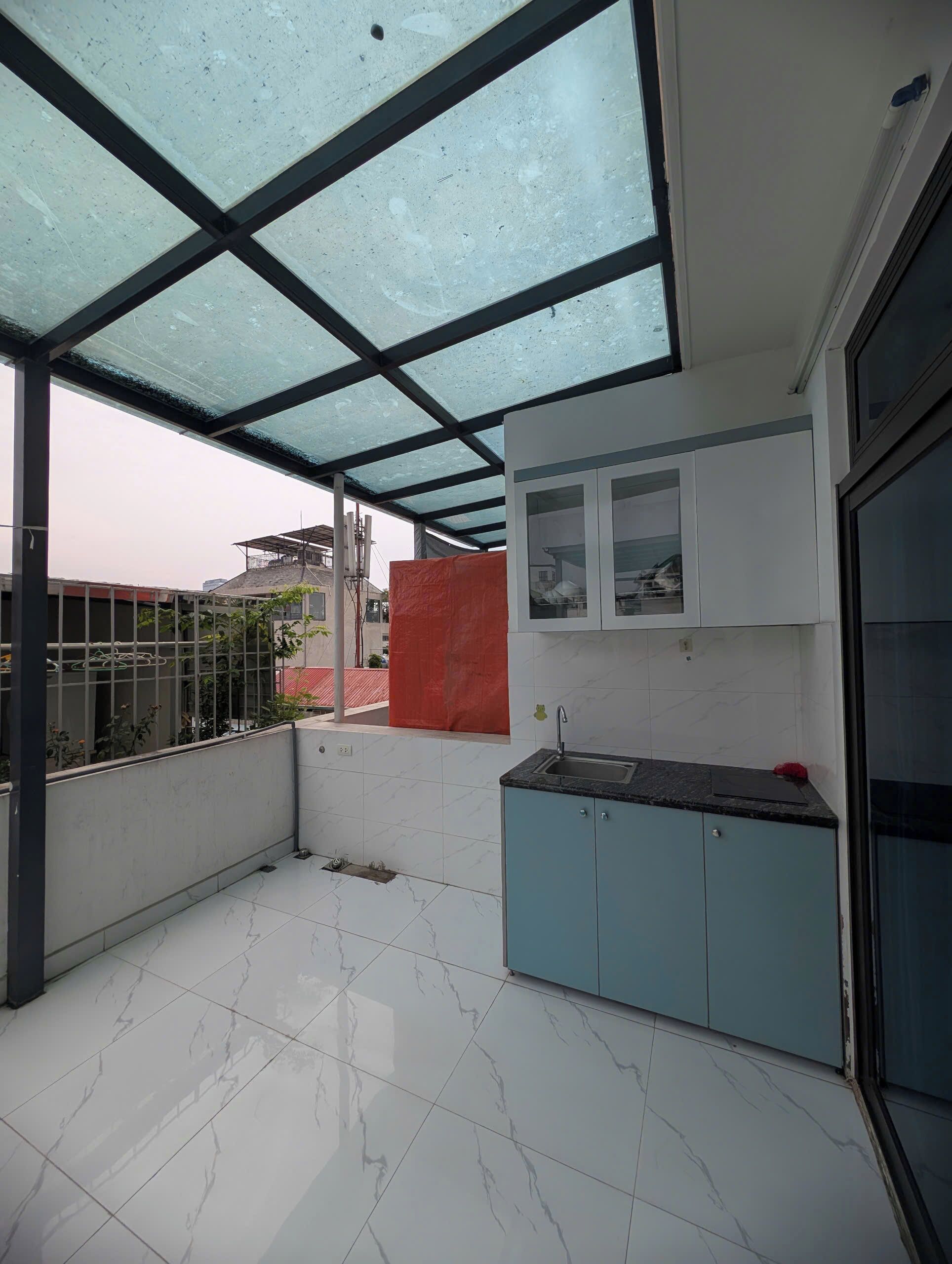 A modern kitchen with a glass ceiling, white marble tiles, and light blue cabinets.
