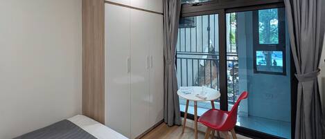 Un dormitorio moderno con cama, armario, una pequeña mesa con silla y un balcón con vistas.