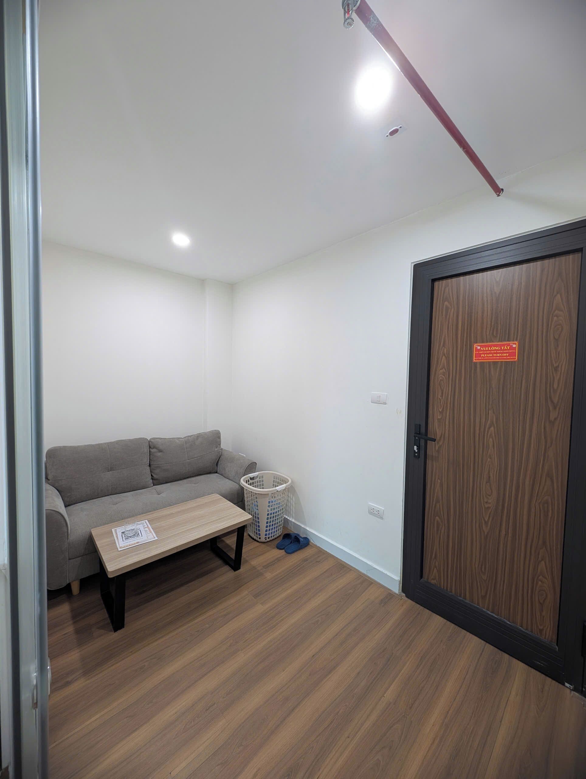 A room with a grey sofa, a wooden table, a laundry basket, and a door with a sign.
