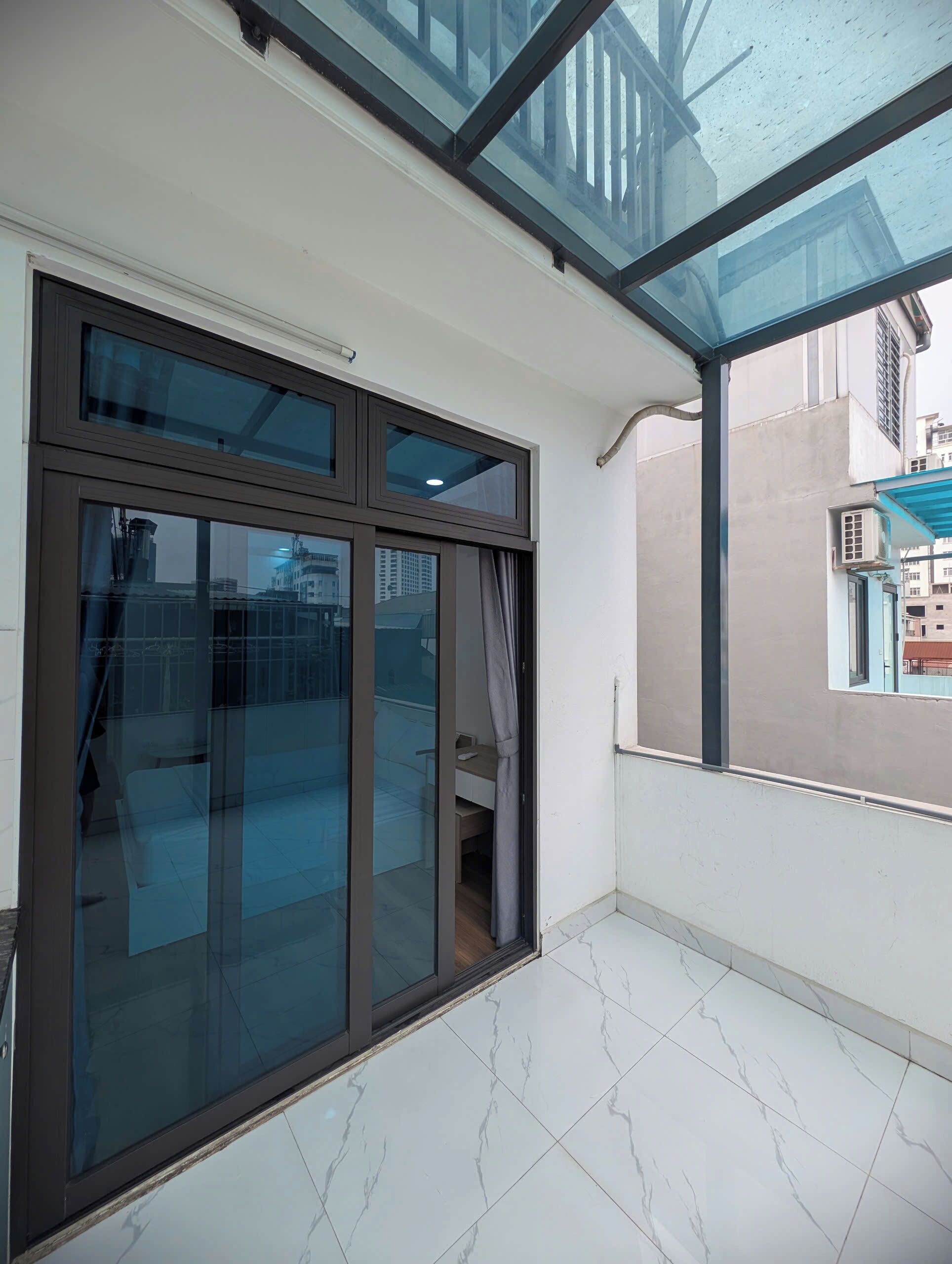 Una stanza con un'ampia porta-finestra scorrevole che dà su un balcone esterno, una scrivania piccola e una sedia.