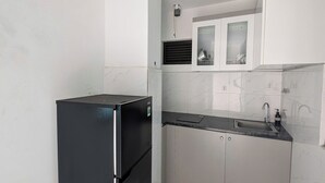 Une cuisine de taille réduite avec des meubles blancs, un réfrigérateur noir et un évier.