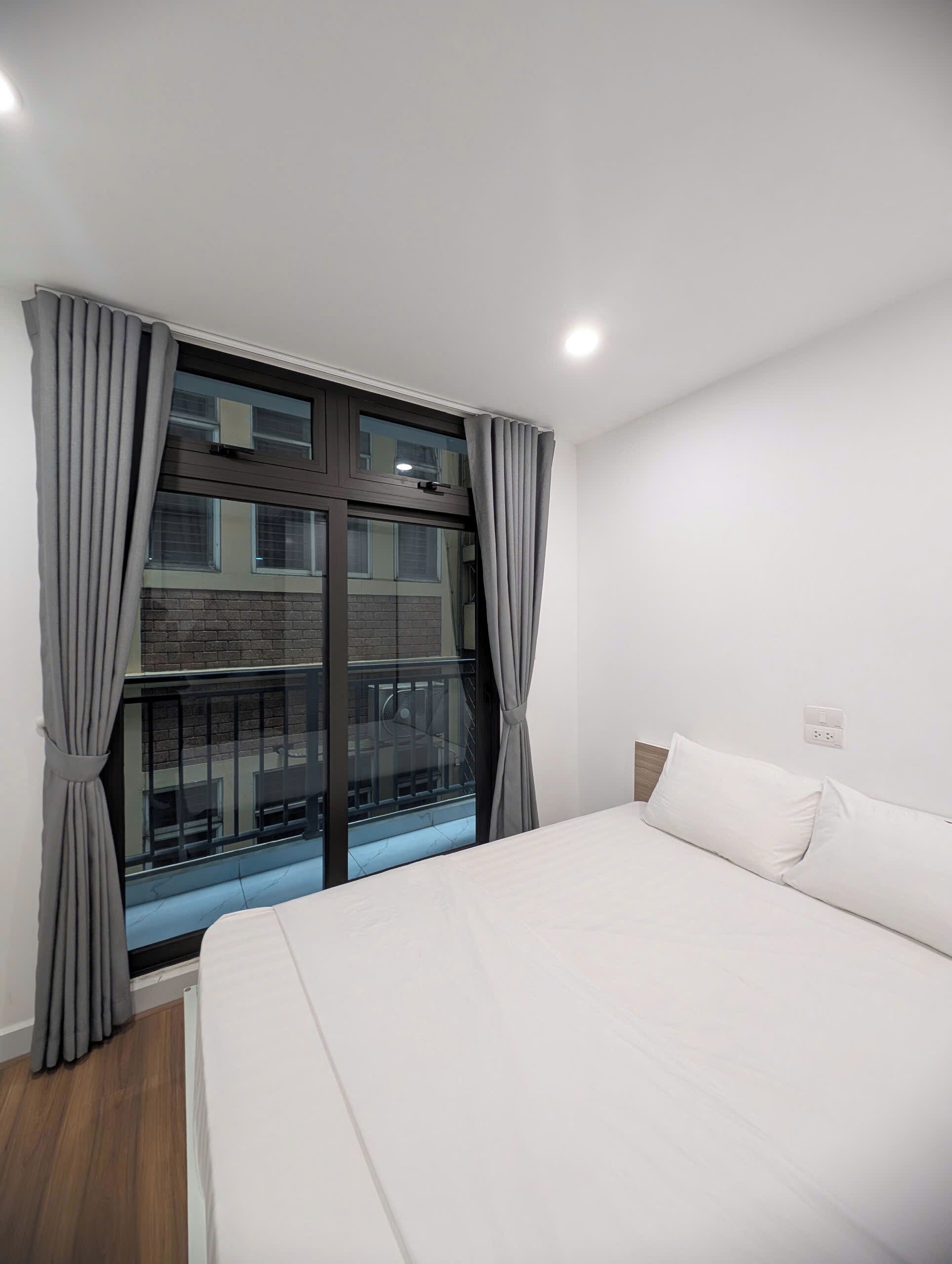 A bedroom with a large bed, a window with curtains, and a view of a building outside.