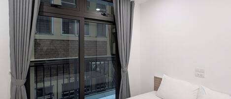 A bedroom with a large bed, a window with curtains, and a view of a building outside.