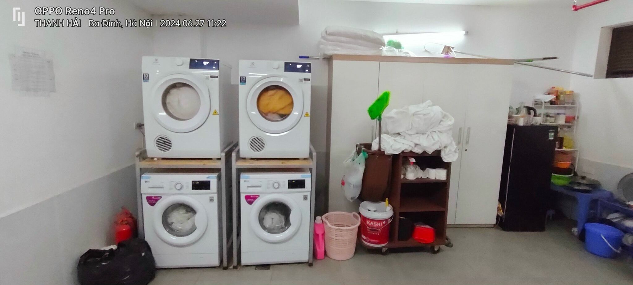 A laundry room with four stacked washing machines, a mop, a shelf with cleaning supplies, and a cabinet.