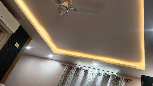 Ein Deckenventilator mit Lampenaufsatz, ein Vorhang mit Muster und ein Bett mit Decke.
