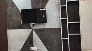 Ein modernes Wohnzimmer mit Fernseher an einer Wand mit geometrischem Muster, einer eingebauten Sitzbank mit Schubladen und einem Regalelement.