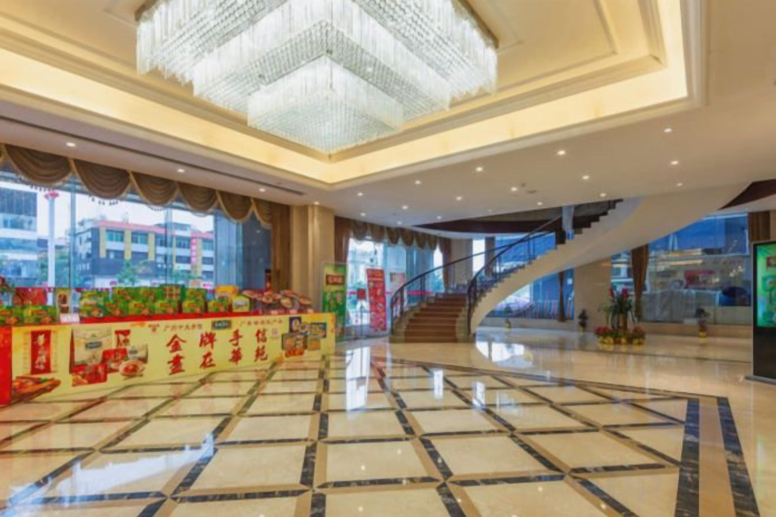 A spacious lobby with a marble floor, a grand chandelier, and a staircase leading to upper floors.