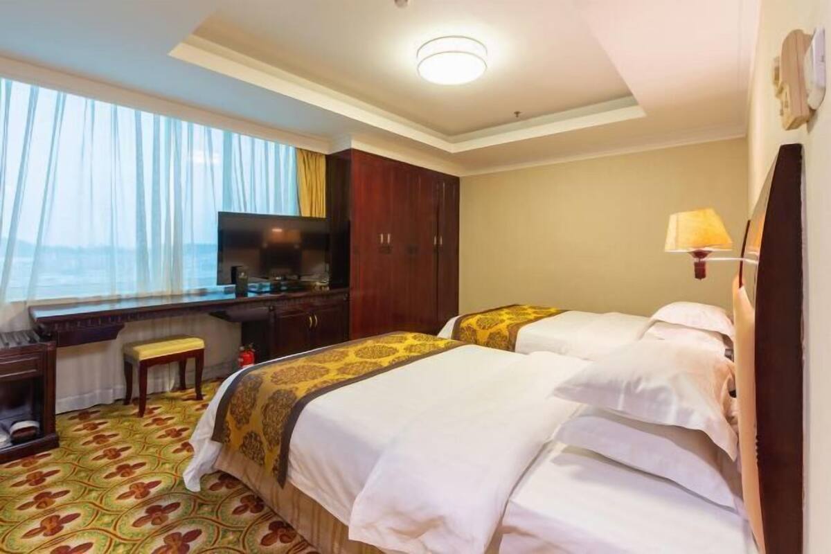 Une chambre d’hôtel avec deux lits, un bureau, une télévision et une fenêtre avec des rideaux.
