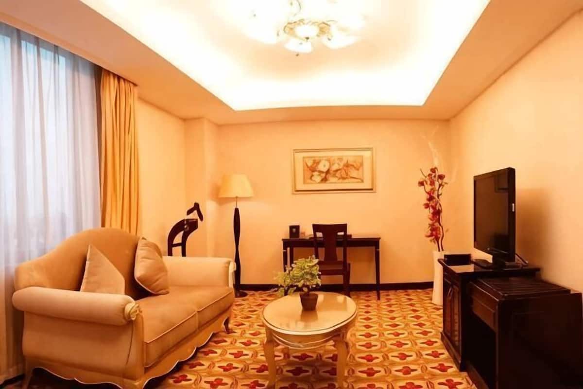 Une chambre d’hôtel avec un canapé, une petite table, un téléviseur, une lampe et un tableau au mur.
