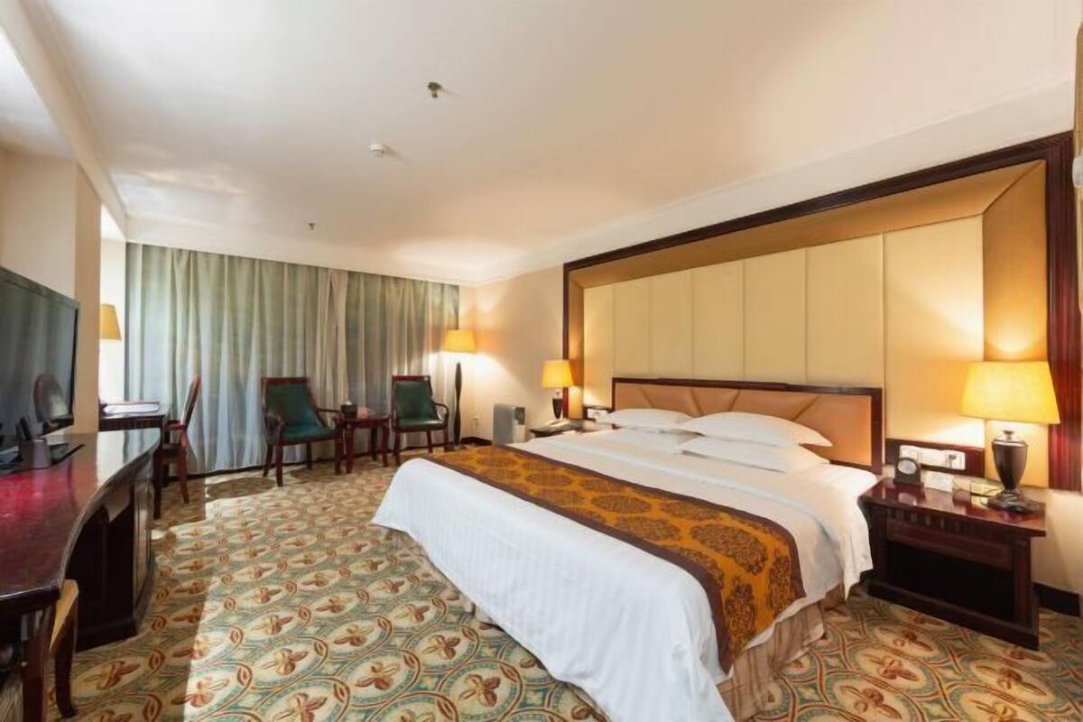 Une chambre d’hôtel avec un grand lit, deux fauteuils, un bureau et un téléviseur.