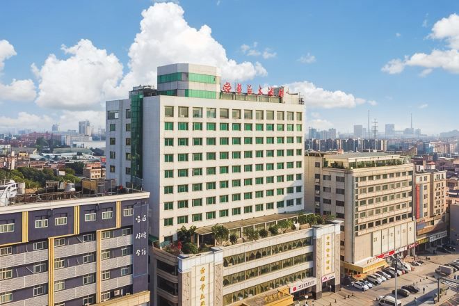Un hotel de varios pisos con una fachada llamativa verde y blanca, varios balcones y un estacionamiento visible al frente.