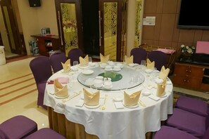 Una mesa redonda preparada para una comida, rodeada de sillas, en una habitación con un papel tapiz decorativo y un televisor.