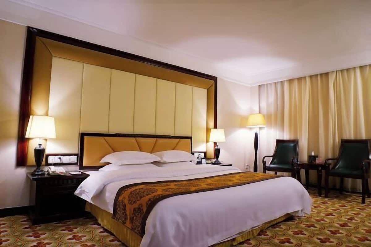 Une chambre d’hôtel avec un grand lit, deux tables de chevet avec des lampes, une chaise et un rideau.