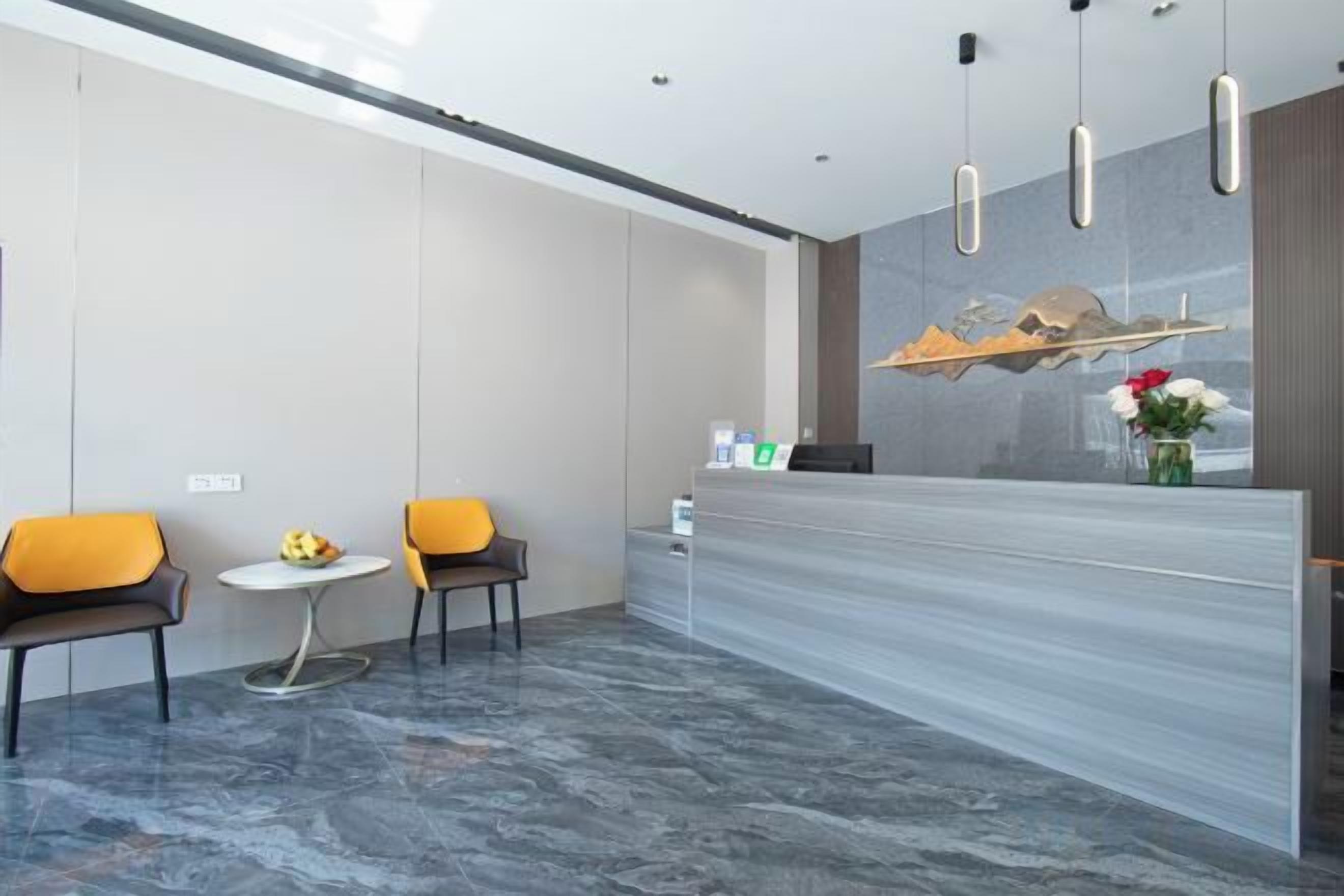 A reception area with a marble floor, two chairs, a small table with a fruit bowl, and a reception desk with a vase of flowers.