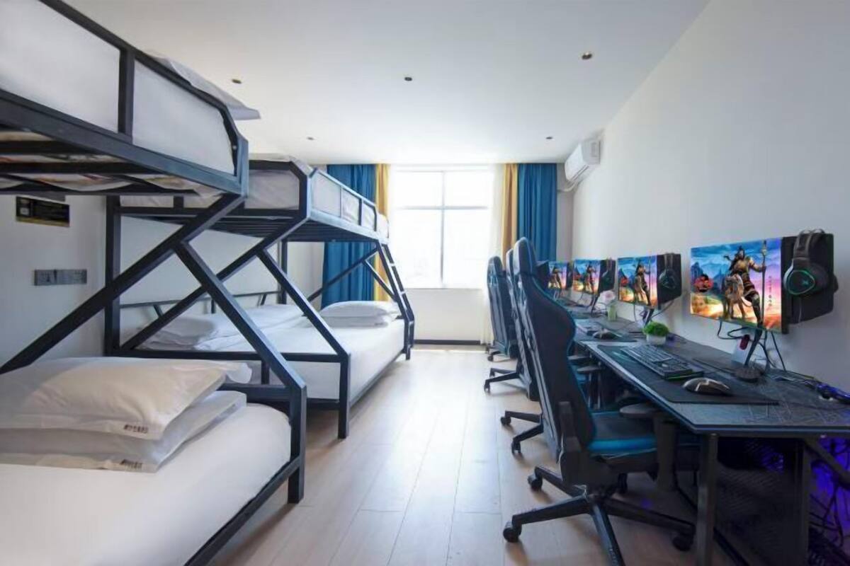 A dormitory room with bunk beds, a desk with a computer, and multiple monitors.
