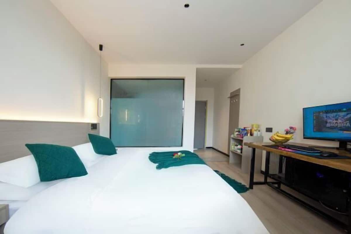 A modern hotel room with a large bed, a television, a desk, and a sliding door leading to a balcony.