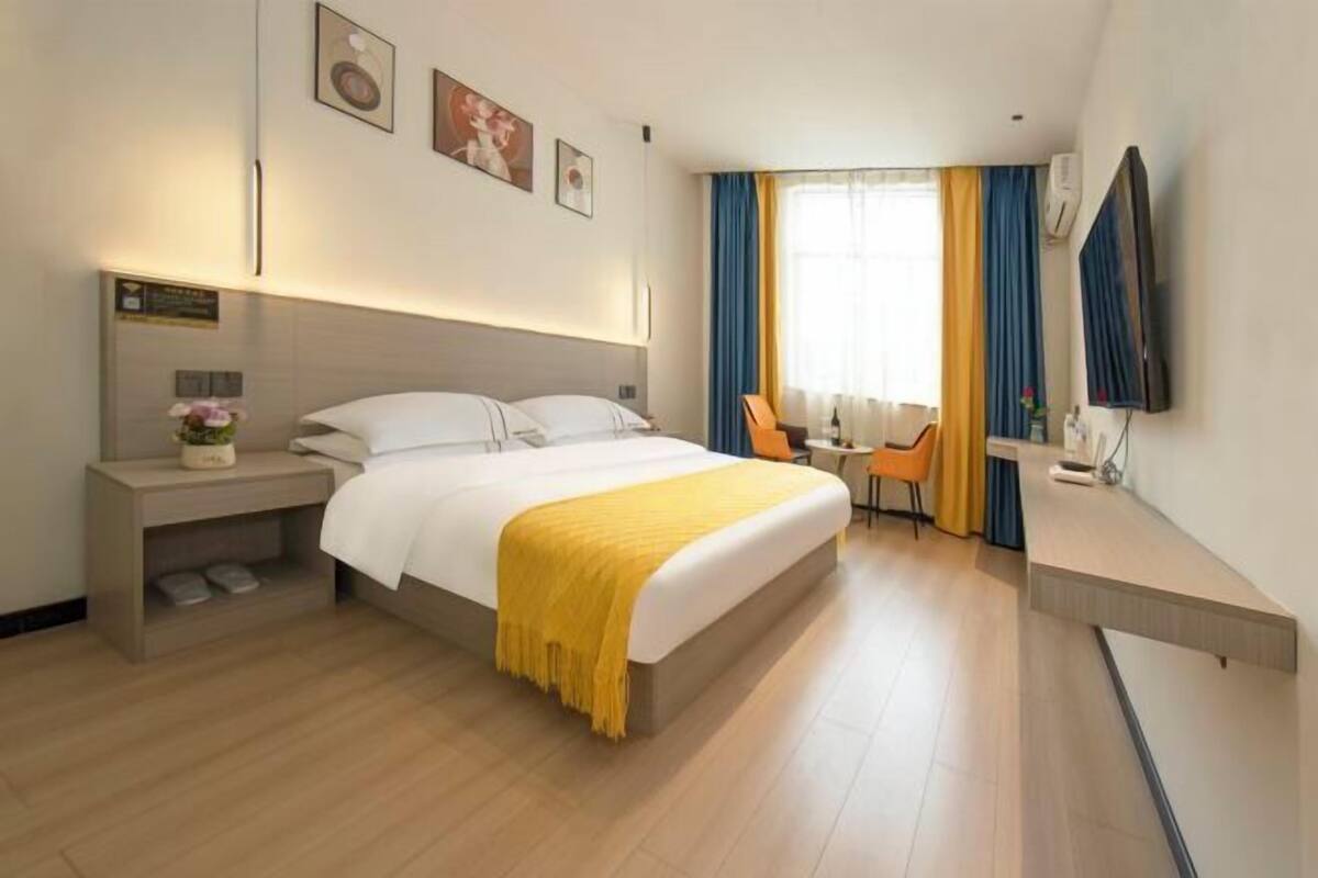 A hotel room with a bed, bedside table, chair, desk, and a TV.