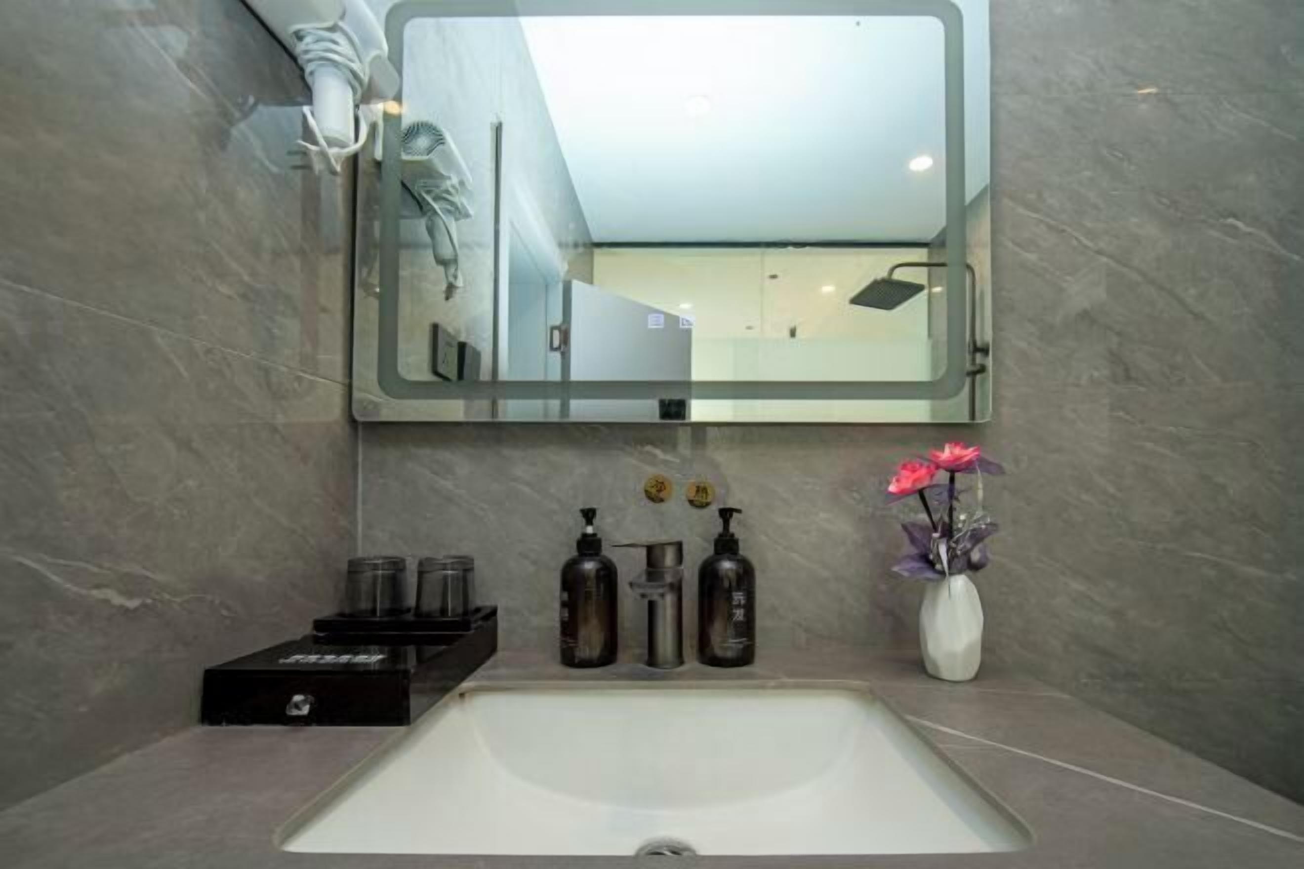A bathroom with a large mirror, a white sink, and a vase with flowers.