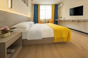 Habitación de hotel con cama, mesita de noche con lámpara, televisor montado en la pared y ventana con cortinas.