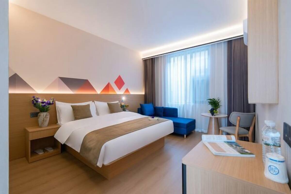 A hotel room with a bed, a desk, a chair, a small table, and a sofa.