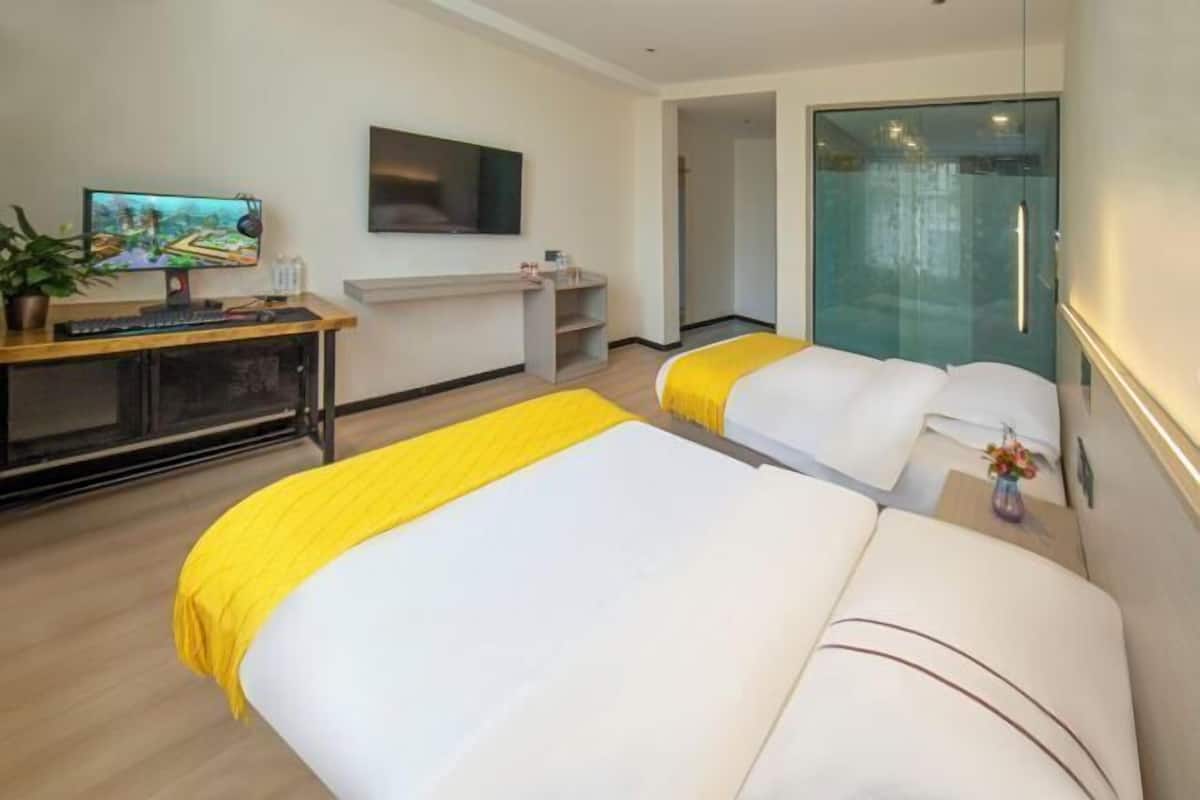 A hotel room with two beds, a desk with a computer, a TV, and a glass-enclosed bathroom.
