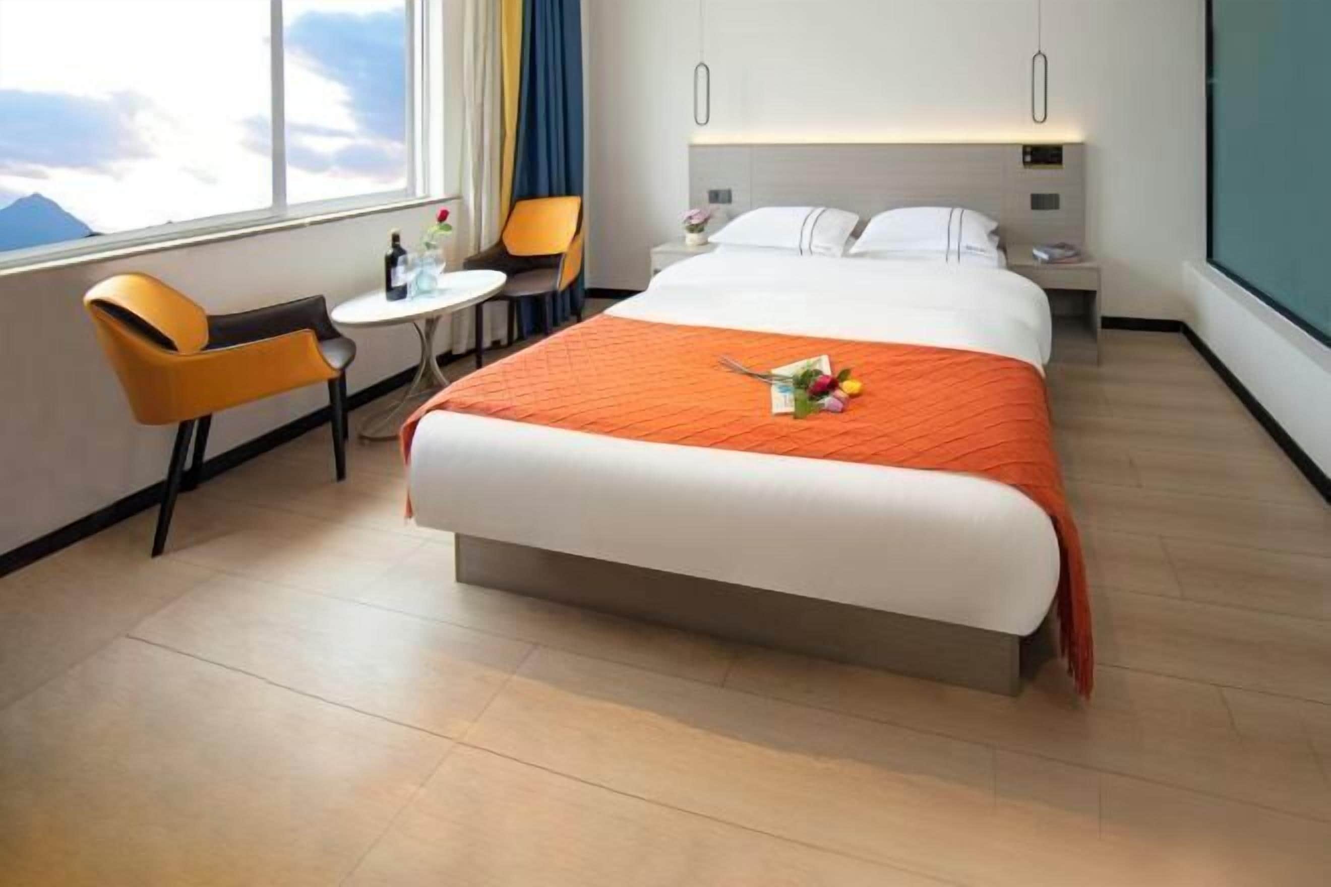 A hotel room with a bed, a small table, a chair, and a window with a view.