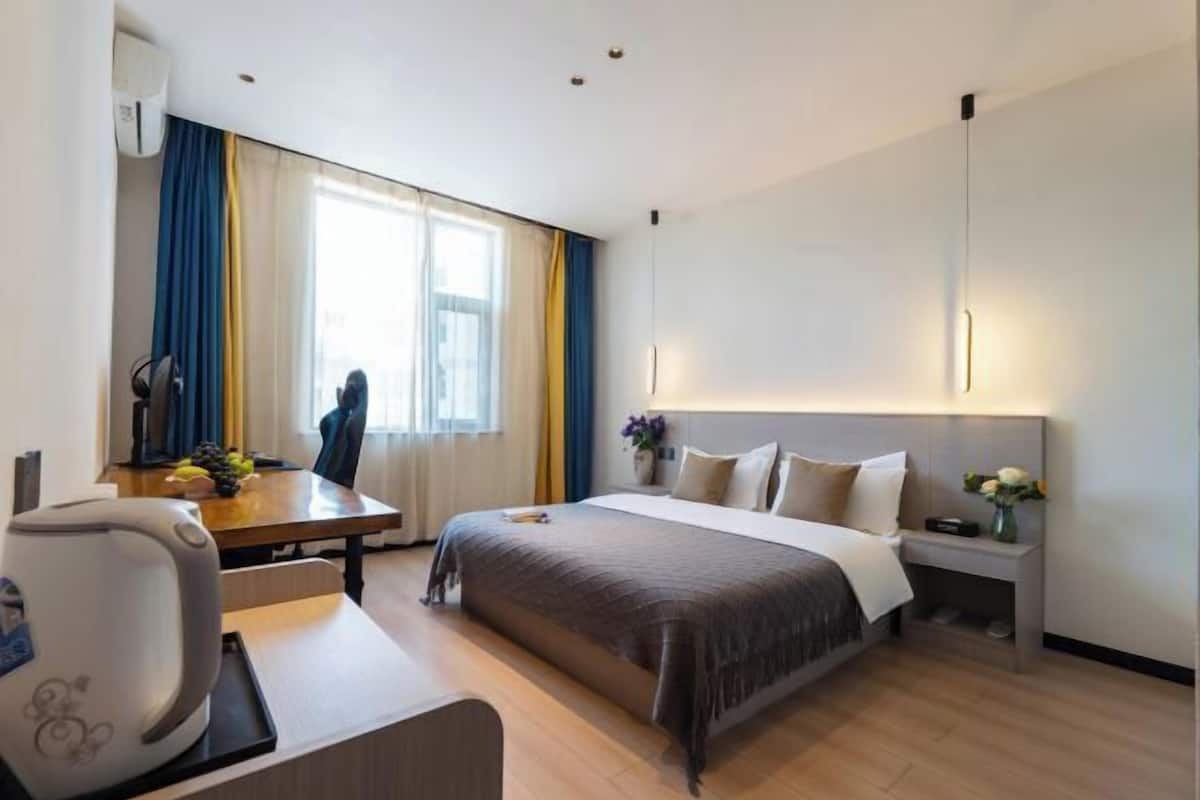 A hotel room with a bed, bedside table, lamp, and a view of the outdoors.