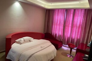 Una habitación de hotel con una cama, un sillón rojo, una mesita y una ventana con cortinas.