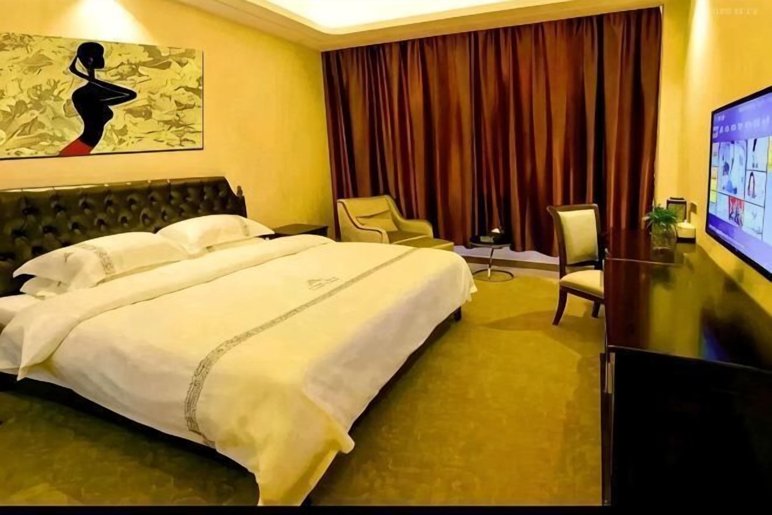 Ein Hotelzimmer mit einem großen Bett, zwei Stühlen, einem Schreibtisch und einem Fernseher.