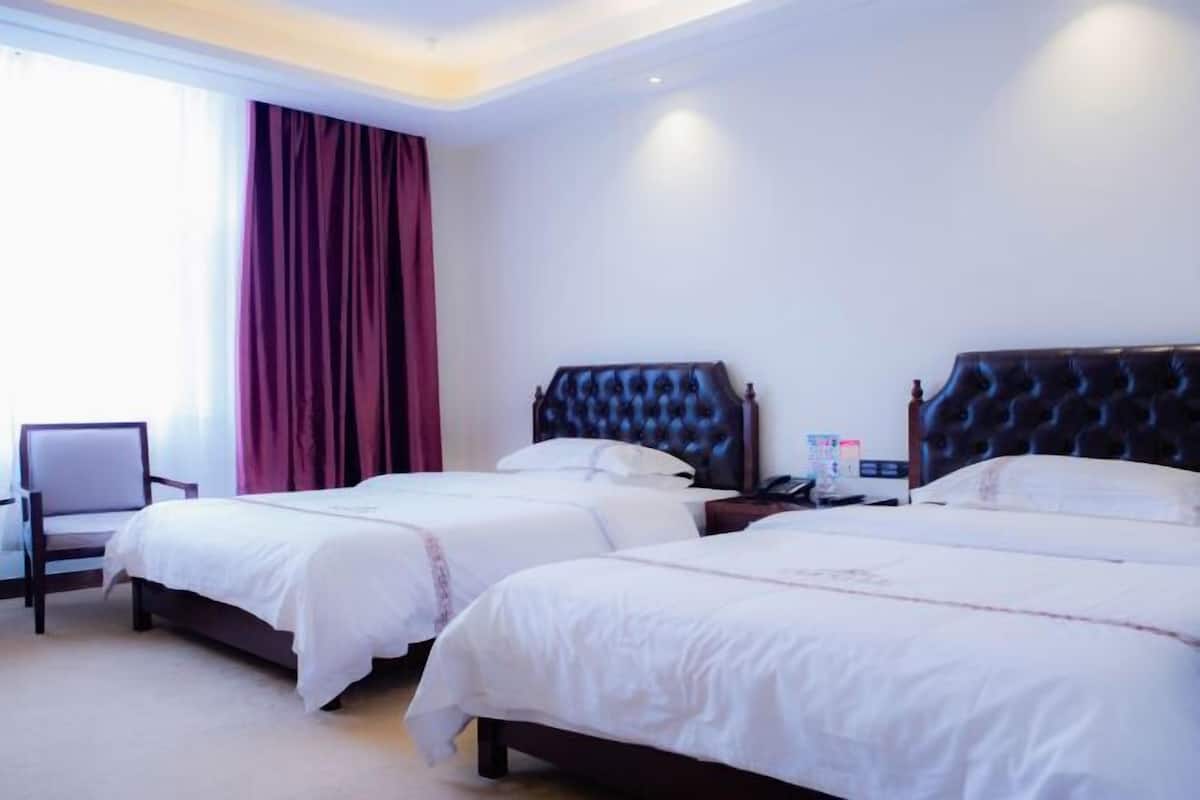 A hotel room with two beds, a chair, and a window with curtains.
