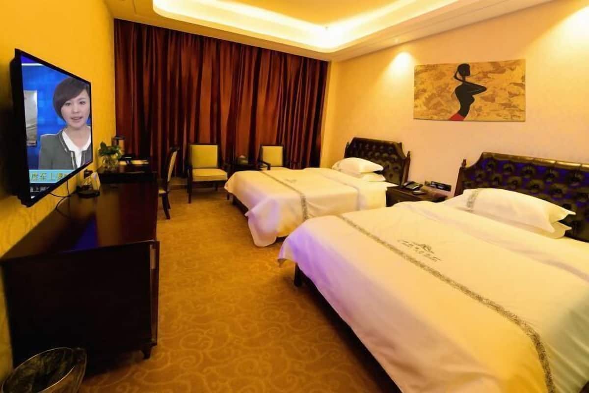 A hotel room with two beds, a television, a desk, and a painting on the wall.