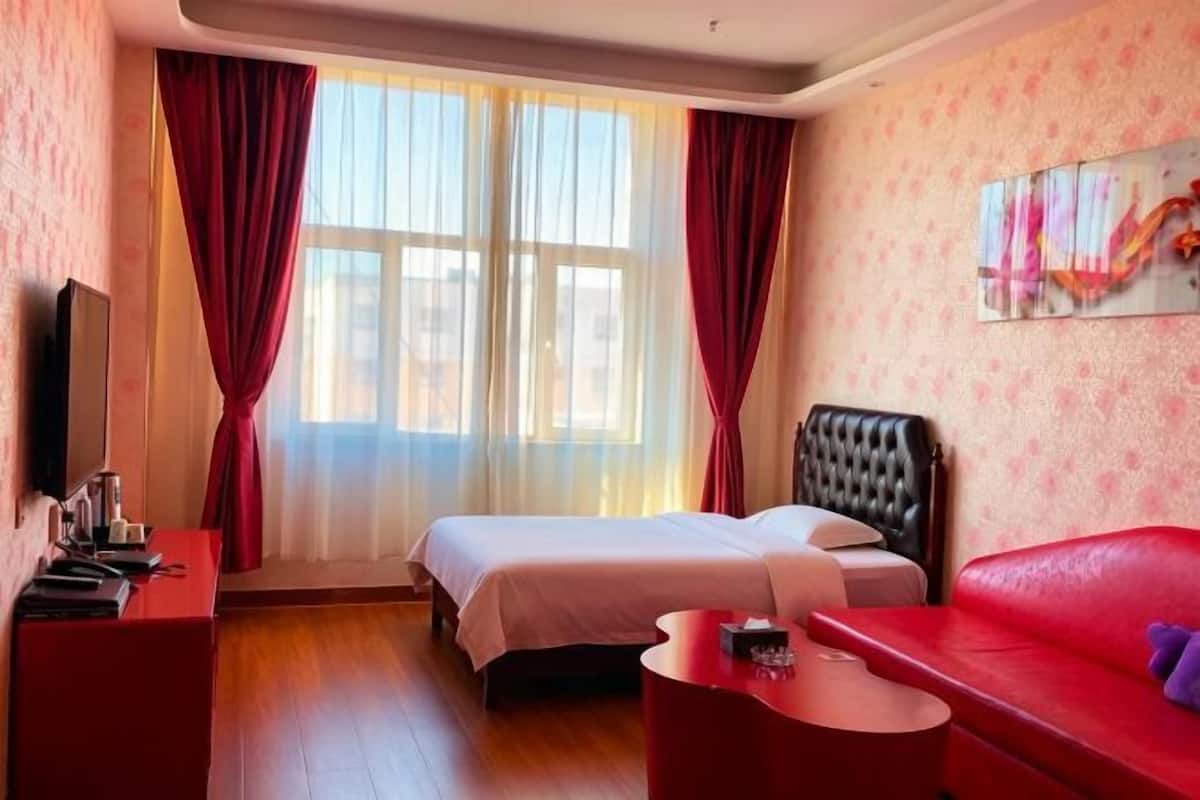 A hotel room with a bed, a red sofa, a TV, and a window with curtains.