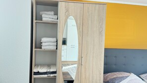 Une chambre avec une armoire en bois, un lit avec une tête de lit grise et un mur jaune.