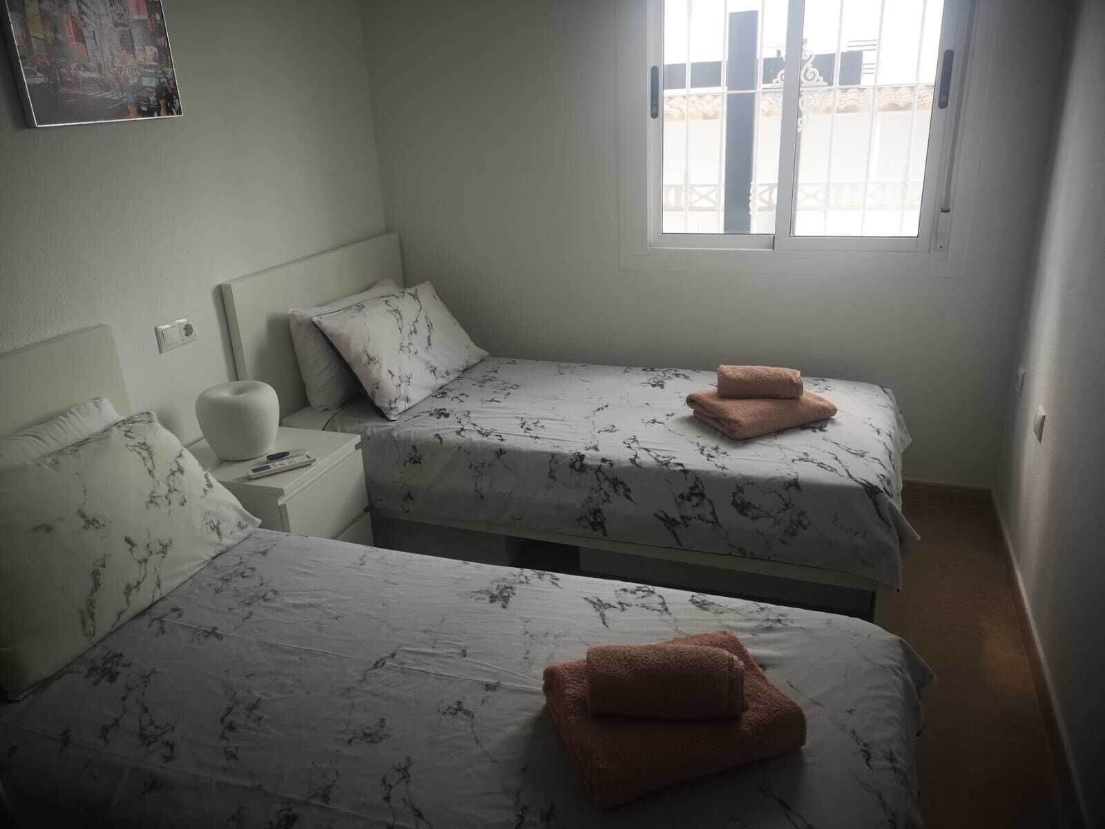 Una habitación pequeña y limpia con dos camas, una mesita de noche y una ventana.