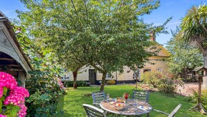 Un tavolo rotondo in legno con quattro sedie, immerso in un rigoglioso giardino.