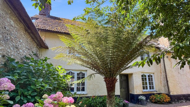 Un edificio tradizionale con tetto in tegole, circondato da una vegetazione rigogliosa e piante fiorite.