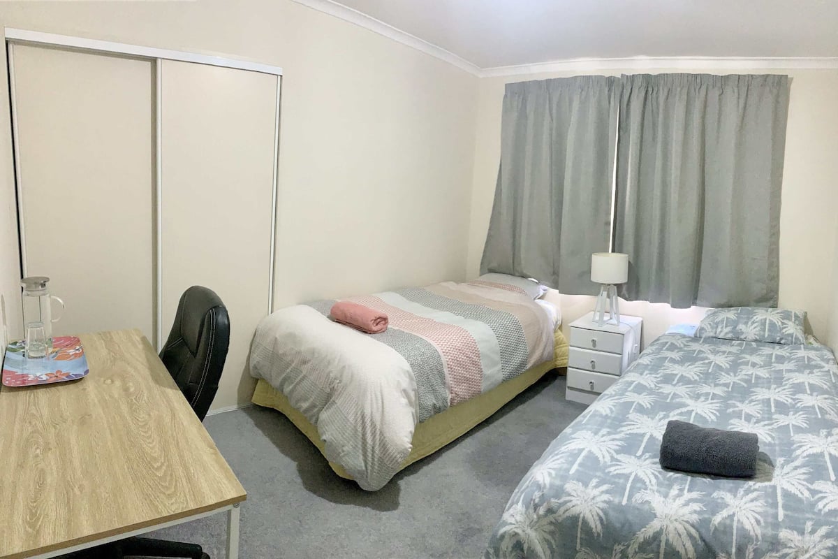 Um quarto com cama, mesa de cabeceira com abajur, cadeira e guarda-roupa.