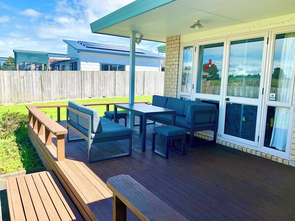 A covered patio with a table and chairs, a wooden bench, and a view of a neighboring house.