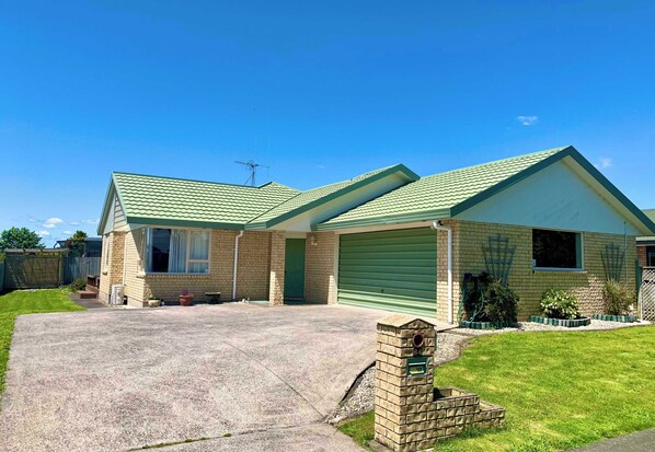 A two-story brick house with a green roof, a garage with a green door, and a well-maintained lawn. - Radiata Homestay (Hamilton)