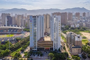 Un edificio de gran altura con diseño moderno, rodeado de otros edificios altos y un estadio.