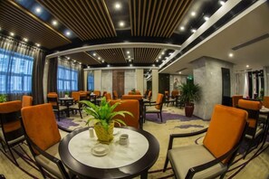 A hotel lobby with round tables, orange chairs, and a large potted plant. - Licheng Youde Hotel (Putian)