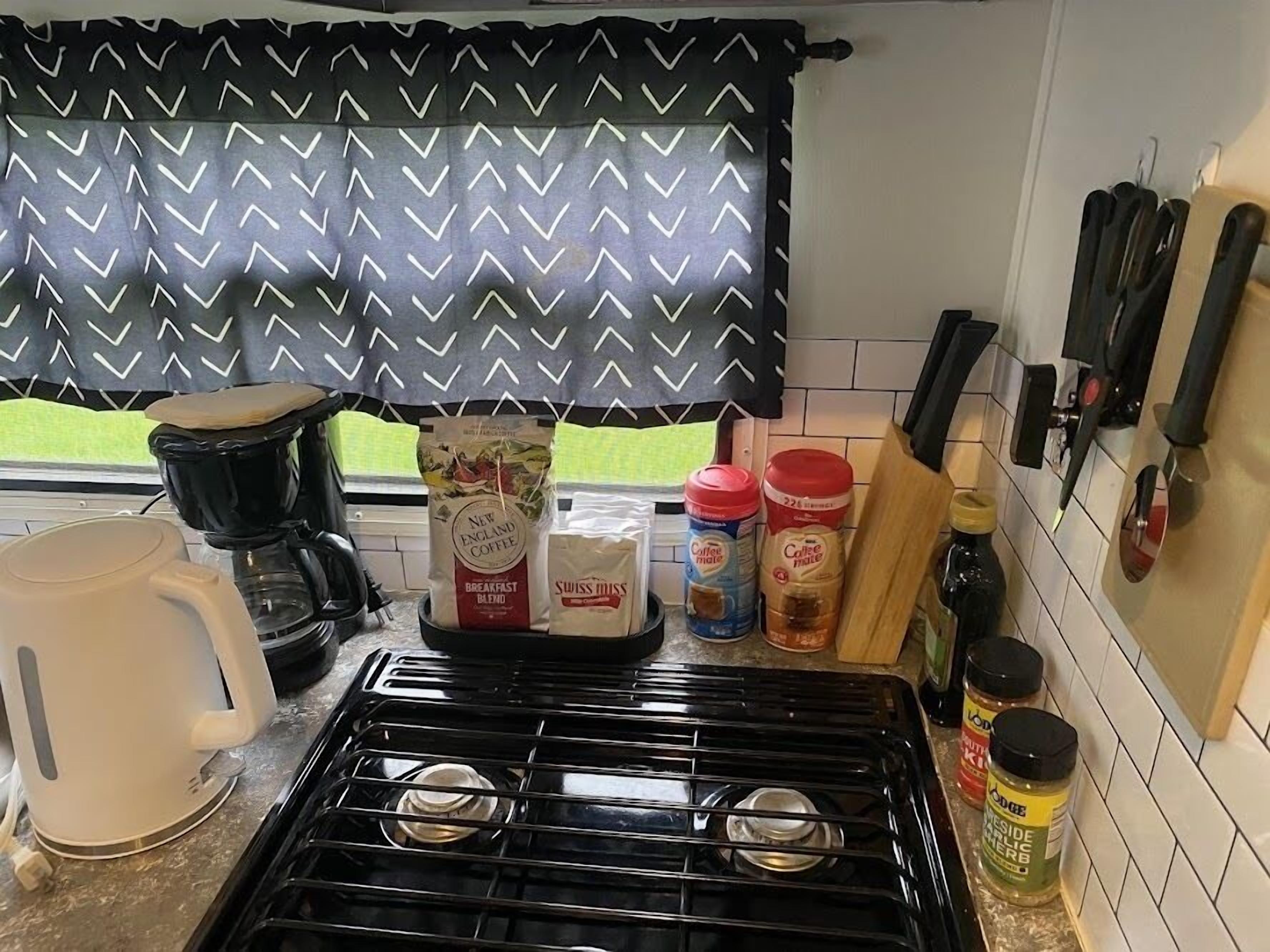Una cocina con estufa a gas, cafetera y varios recipientes de café y especias.